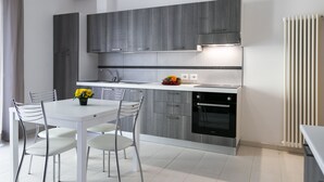 A modern kitchen with grey cabinets, a white countertop, and a black oven. There is a dining table with four chairs and a vase of yellow flowers. - Residenza Riva Azzurra (Rimini)