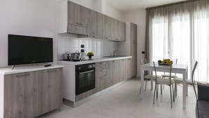 A modern kitchen with a built-in oven, a dining table with chairs, and a TV on a cabinet. - Residenza Riva Azzurra (Rimini)