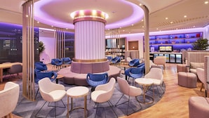 Een moderne lounge met een centraal, rond zitgedeelte, een bar met planken vol decoratieve objecten, en een televisiescherm.