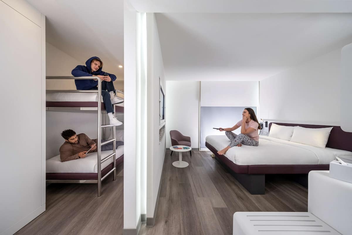 Une chambre d’hôtel moderne avec un lit superposé, un canapé, une petite table ronde et un grand lit.