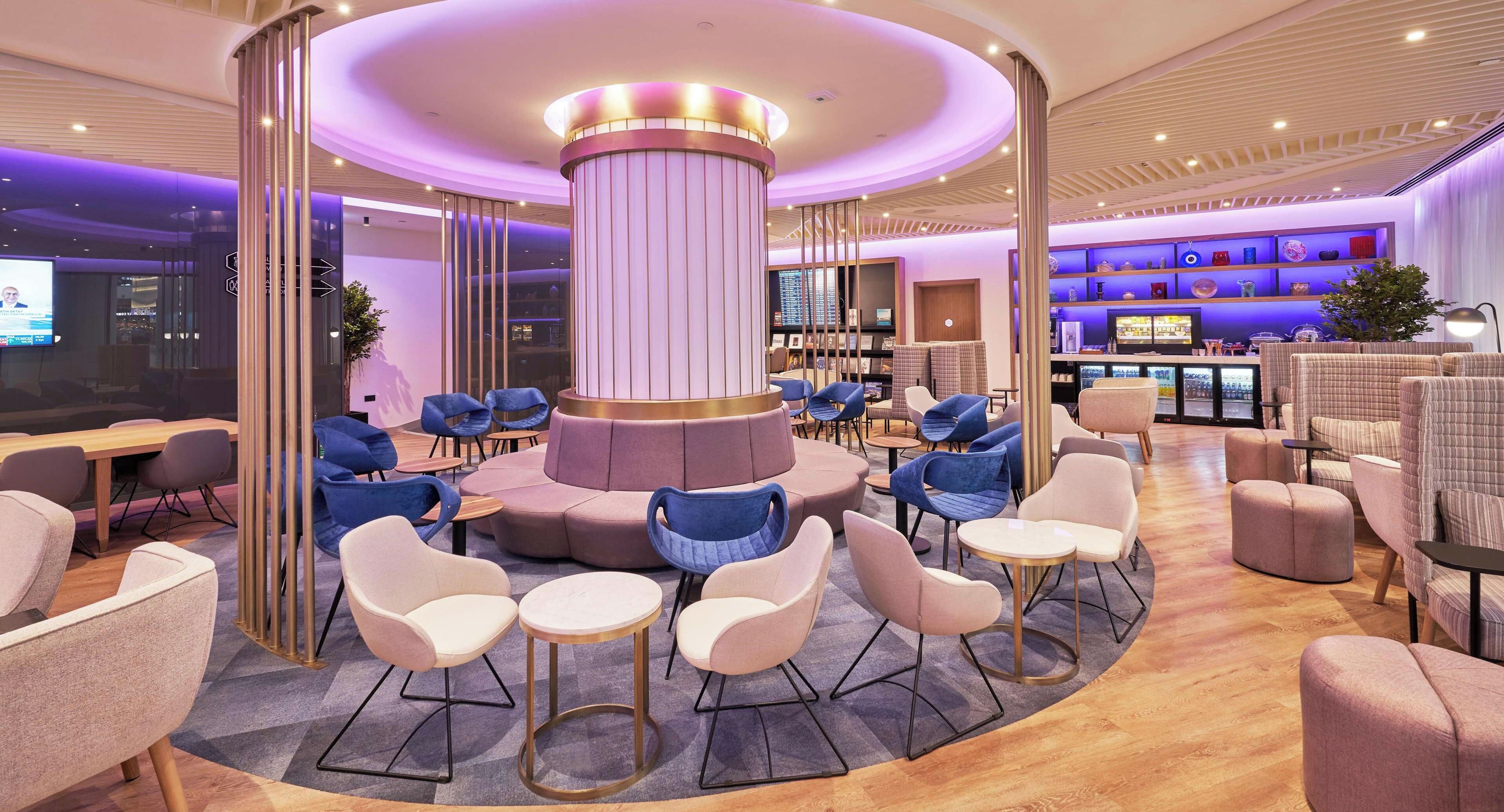 A modern lounge area with a central column, seating arrangements, and a bar area with shelves.