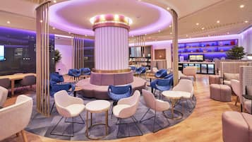 Ein moderner Lounge-Bereich mit einer zentralen Säule, Sitzgruppen und einer Bar mit Regalen.