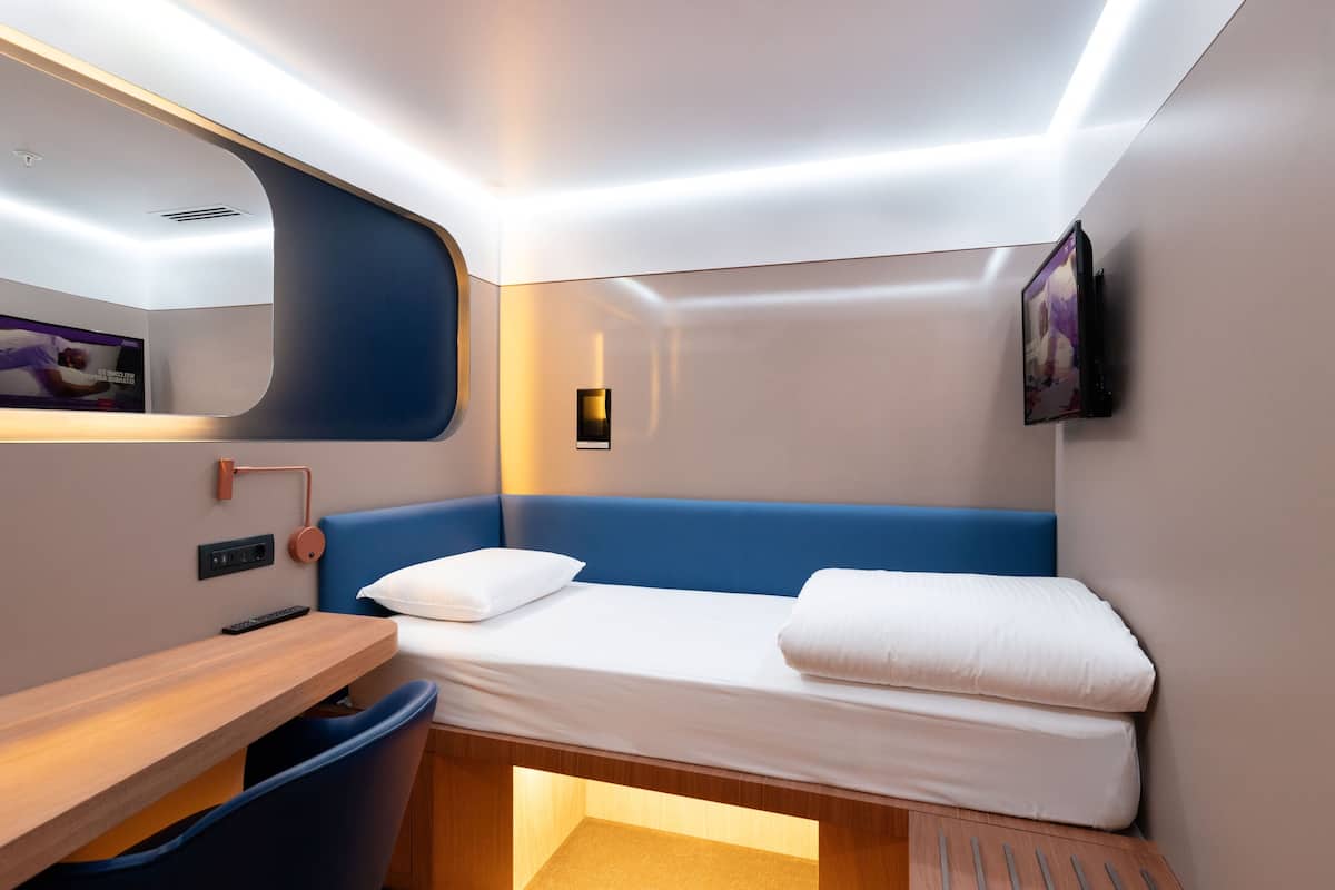 Une chambre moderne et compacte, équipée d’un lit, d’un bureau et d’une chaise.