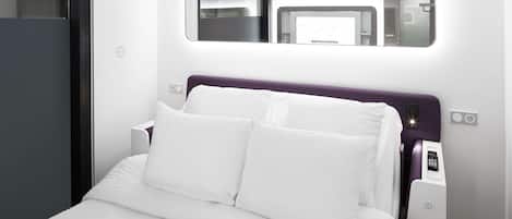 Una camera d'albergo moderna con un letto rifatto, un comodino, uno specchio e un pannello di controllo.