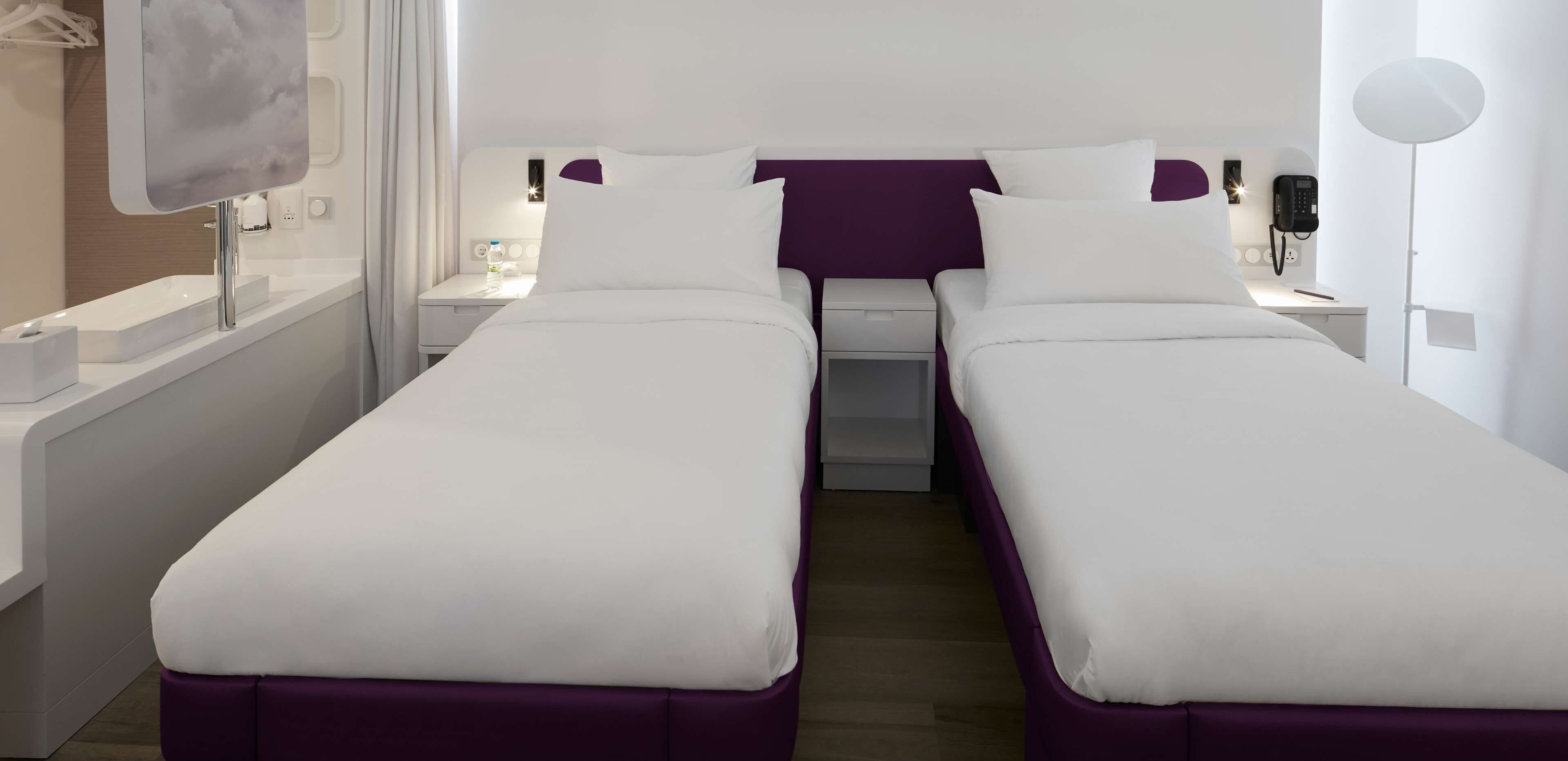 Habitación de hotel con dos camas individuales, una mesita de noche con lámpara, teléfono y un pequeño atril.