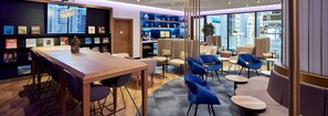 A modern hotel lobby with a wooden reception desk, seating area with blue chairs, and a digital display board. - YOTELAIR Istanbul Airport AIRSIDE (Arnavutköy)