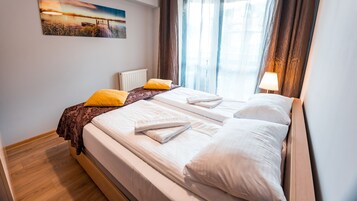 Cama doble con sábanas blancas, cabecera de madera y vista a un lago tras cortinas traslúcidas.