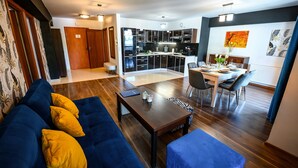 A modern living room with a blue sofa, a wooden coffee table, and a dining area with a table set for four. - Sun & Snow Centrum Piłsudskiego (Krynica-Zdroj)