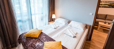 A hotel room with a bed, a nightstand, a lamp, a sofa, and a painting on the wall.