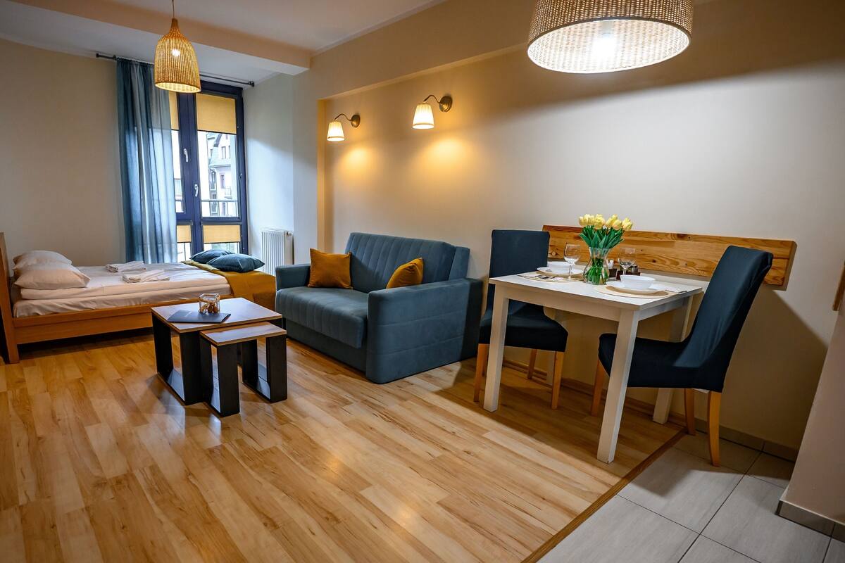 A modern, well-lit room with a bed, sofa, dining table, and chairs.