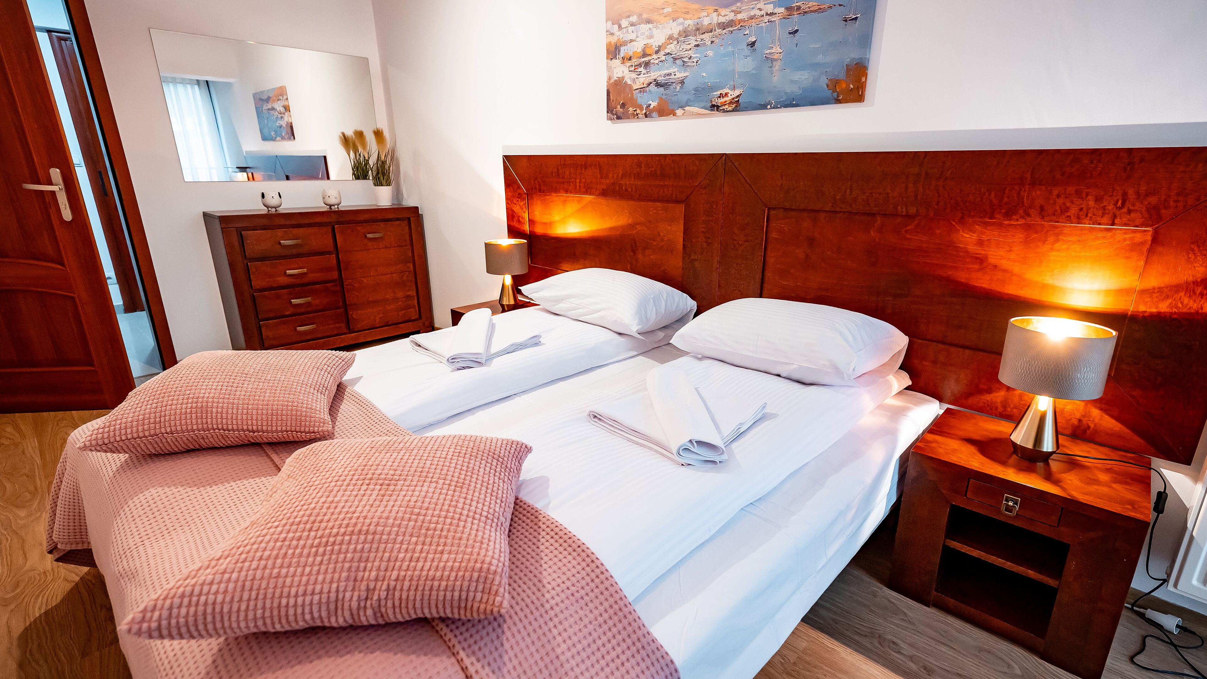 Ein Hotelzimmer mit zwei Betten, einem Holzkopfteil, Nachttischlampen, einem Schminktisch und einem Gemälde an der Wand.