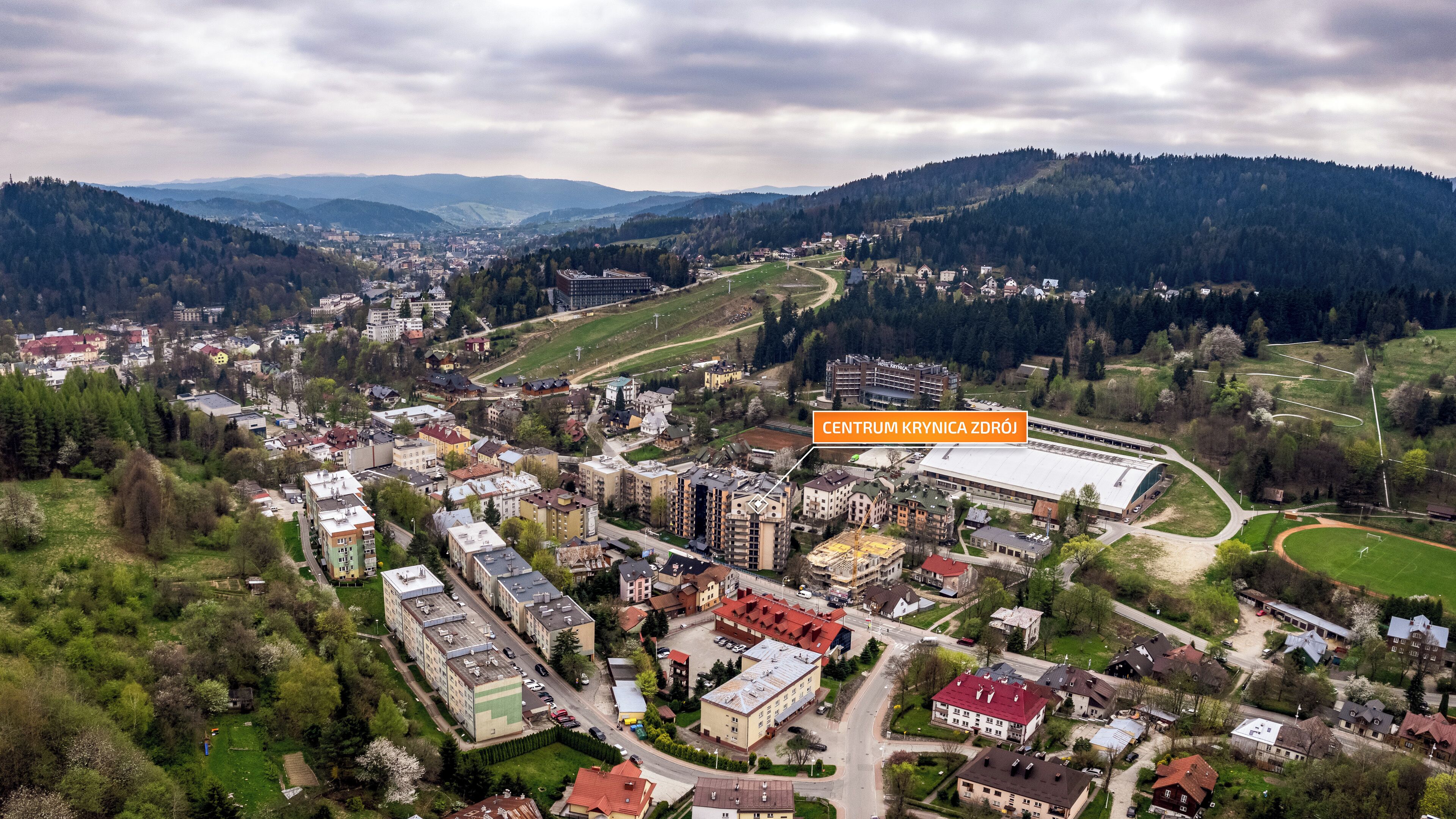 An aerial view of a town with a large sports stadium, surrounded by residential buildings and greenery.