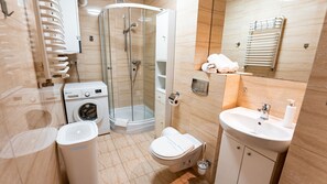 Un baño pequeño con ducha acristalada, lavadora, inodoro y lavamanos.