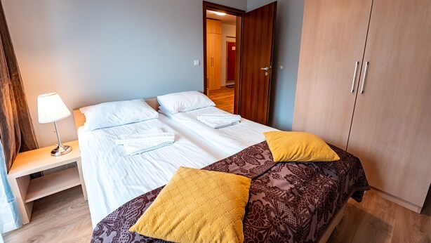A neatly made bed with white linens and two yellow pillows, a bedside table with a lamp, and a wardrobe with two doors. - Sun & Snow Centrum Piłsudskiego (Krynica-Zdroj)