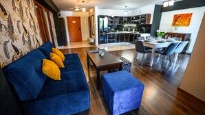 A modern living room with a blue sofa, a dining area with a table and chairs, and a kitchen in the background. - Sun & Snow Centrum Piłsudskiego (Krynica-Zdroj)