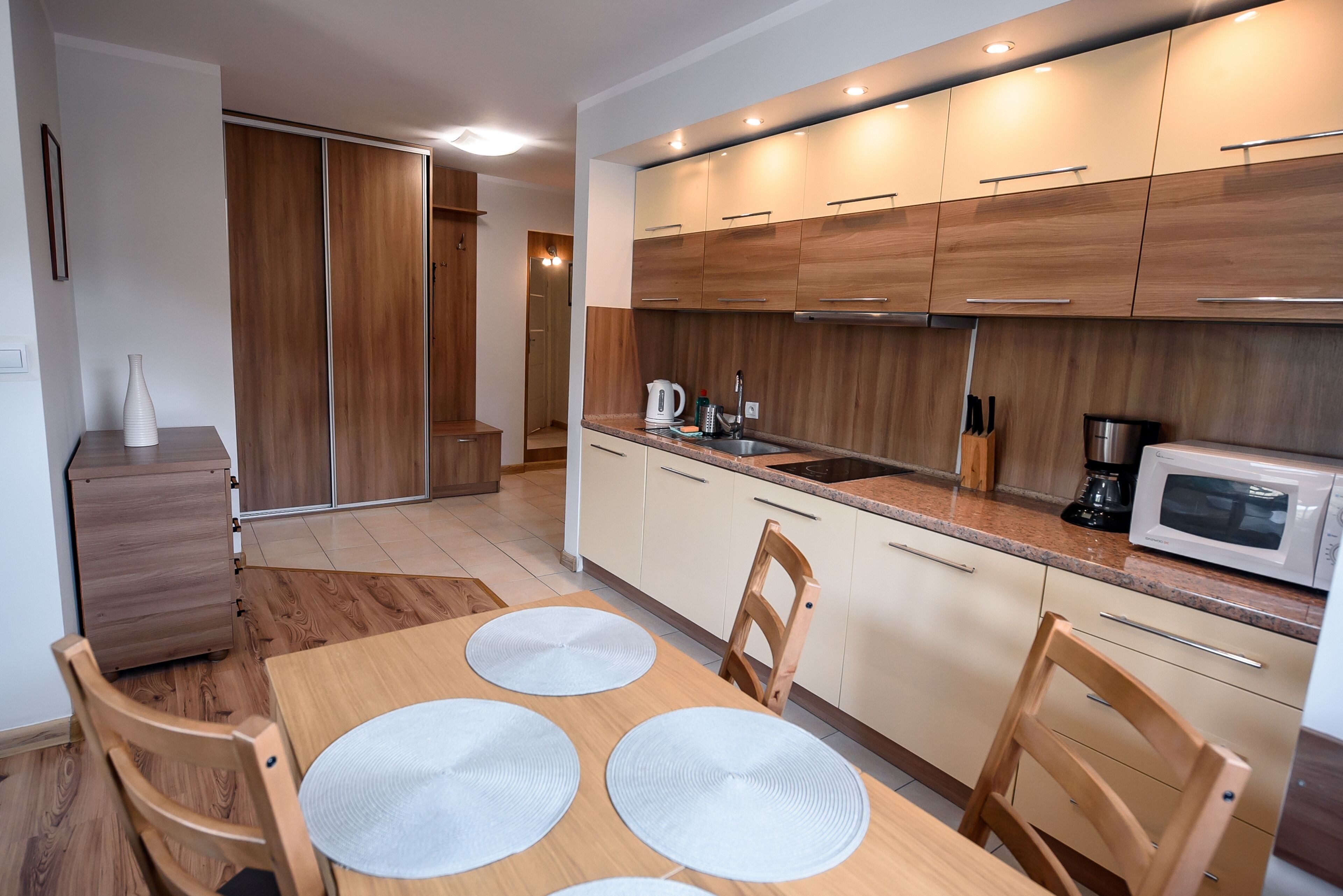 A modern kitchen with wooden cabinets, a dining table with placemats, and a microwave.