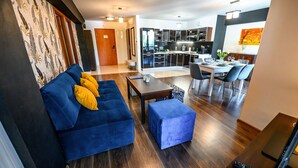 A modern living room with a blue sofa, a small table, and a dining area with chairs. - Sun & Snow Centrum Piłsudskiego (Krynica-Zdroj)