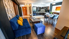 A modern living room with a blue sofa, a small table, and a dining area with chairs. - Sun & Snow Centrum Piłsudskiego (Krynica-Zdroj)