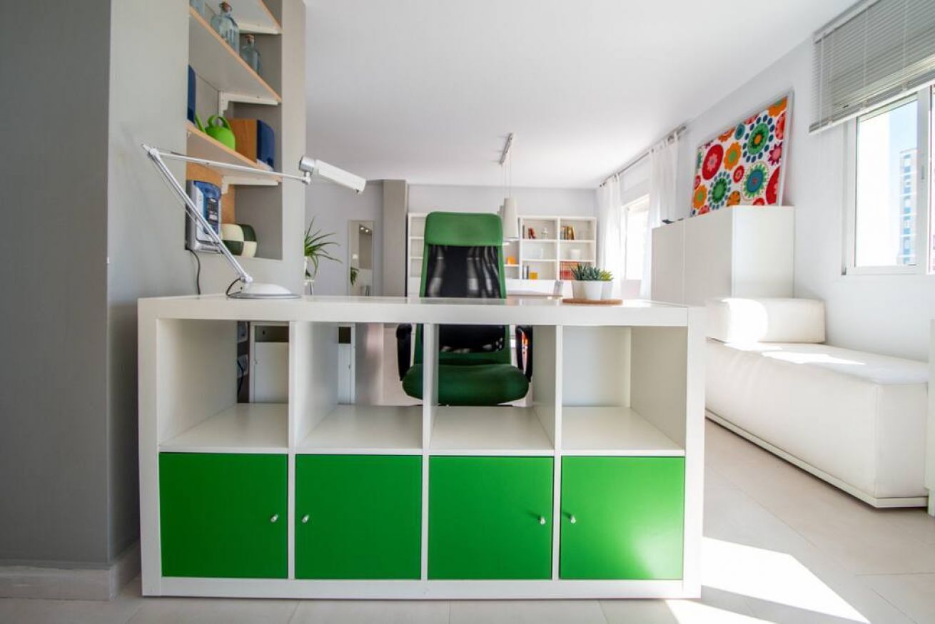 A modern living room with a white sofa, a green and white cabinet, and a colorful abstract painting on the wall.