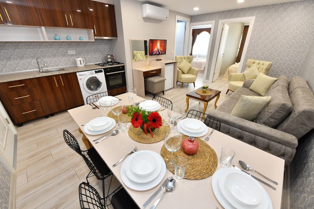 Una cocina moderna con armarios de madera, lavadora integrada y un comedor listo para una comida, con una mesa preparada para cuatro.