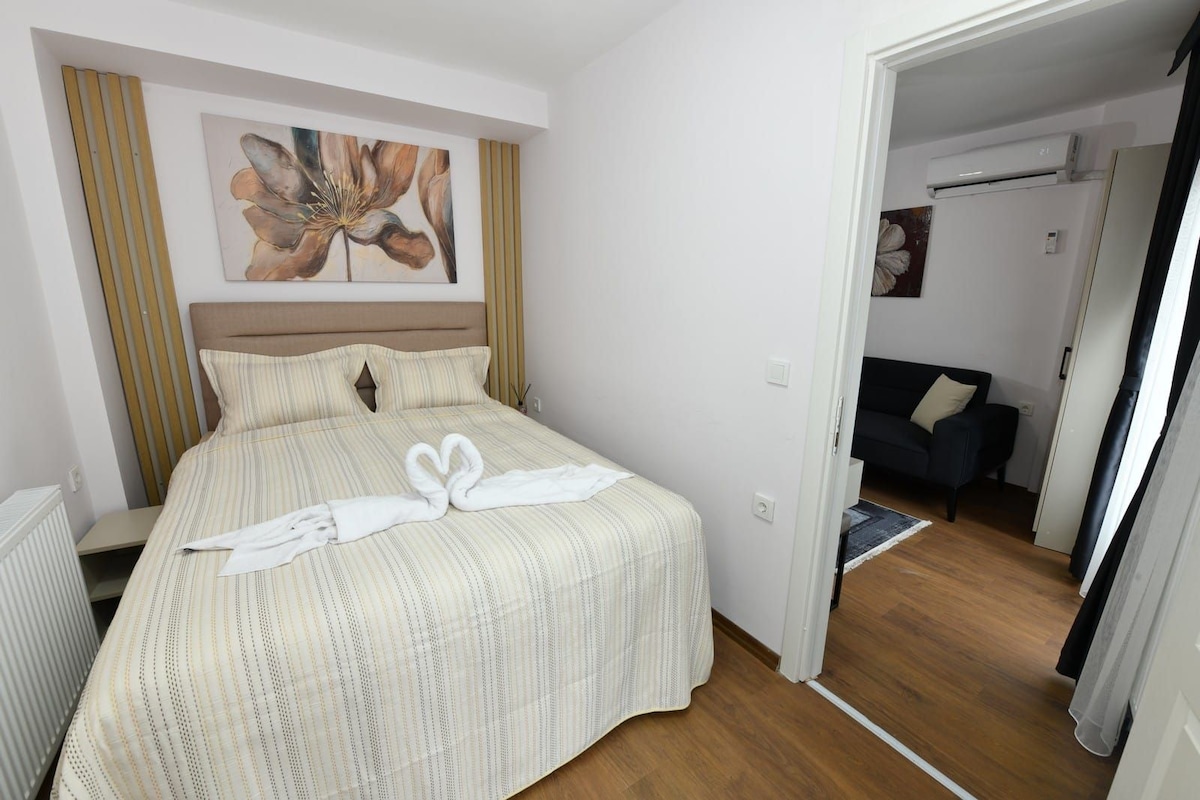 A hotel room with a bed, a painting on the wall, and a view into the living area.
