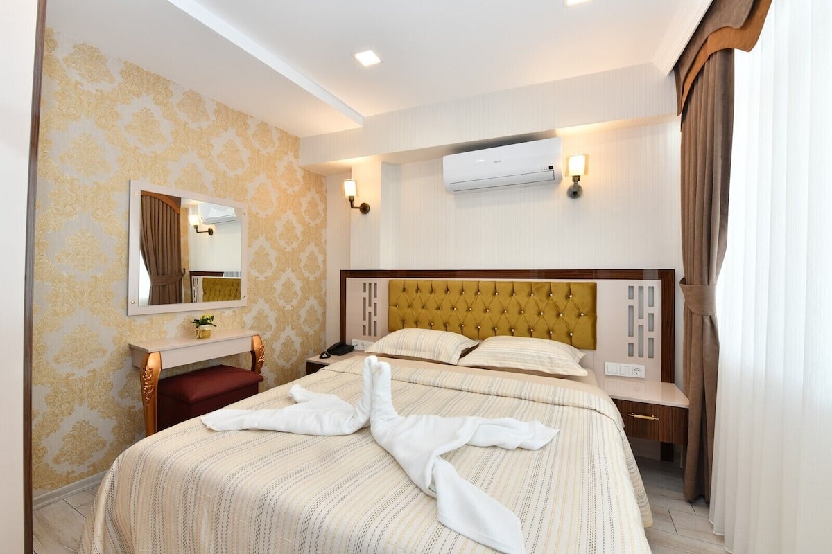 Una habitación de hotel con cama, escritorio, espejo, equipo de aire acondicionado y lámpara.