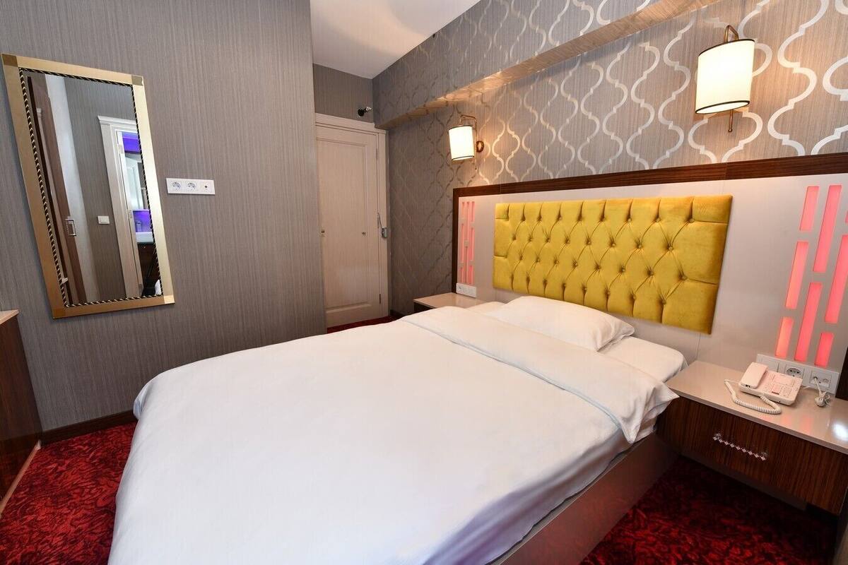 Habitación de hotel con una cama grande, una mesita de noche con teléfono y un espejo en la pared.