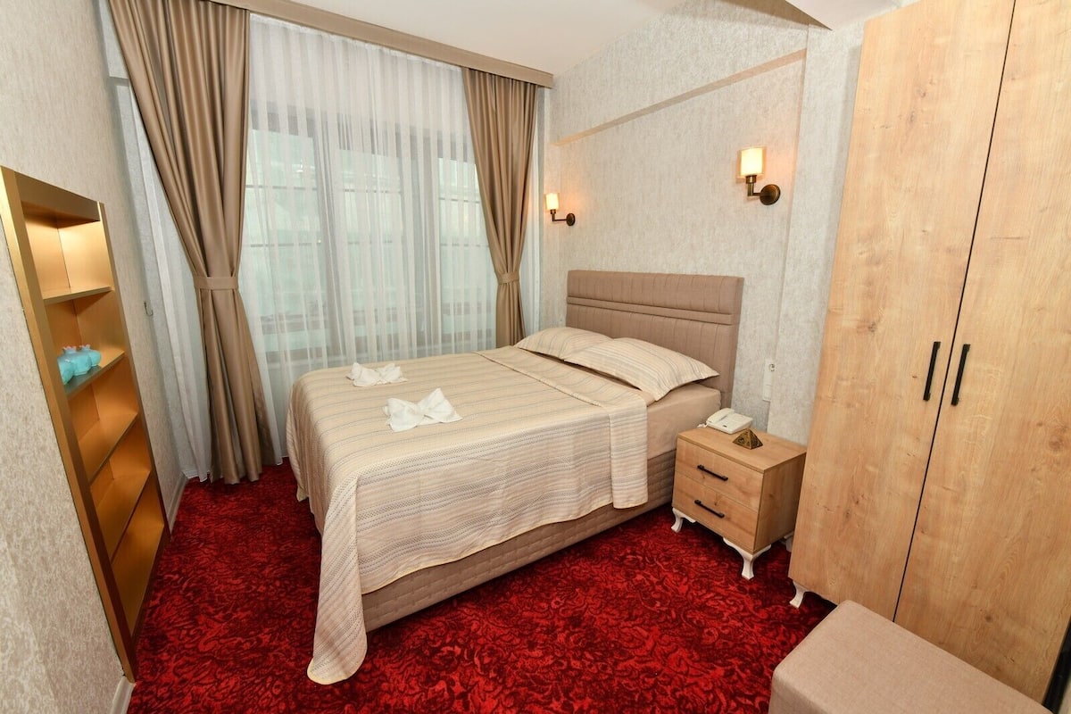 Una habitación de hotel con cama, mesita de noche, armario y alfombra roja.
