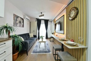A modern living room with a sofa, a dining table, and a TV. There is a potted plant and a clock on the wall. - Sea Moon Hotel (Istanbul)