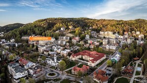 An aerial view of a town with a mix of residential and commercial buildings, surrounded by forested hills. - Apartamenty Sun & Snow Centrum Cicha (Krynica-Zdroj)
