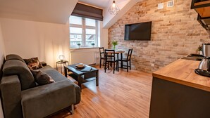 A modern living room with a sofa, a dining table with chairs, a coffee machine, and a TV mounted on a brick wall. - Apartamenty Sun & Snow Centrum Cicha (Krynica-Zdroj)