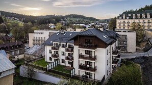 A modern multi-story residential building with balconies, a flat roof, and a view of a hilly landscape in the background. - Apartamenty Sun & Snow Centrum Cicha (Krynica-Zdroj)
