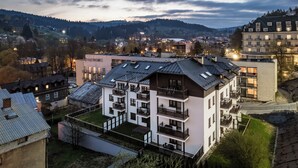 A multi-story residential building with balconies and a flat roof, surrounded by other buildings and a hilly landscape in the background. - Apartamenty Sun & Snow Centrum Cicha (Krynica-Zdroj)