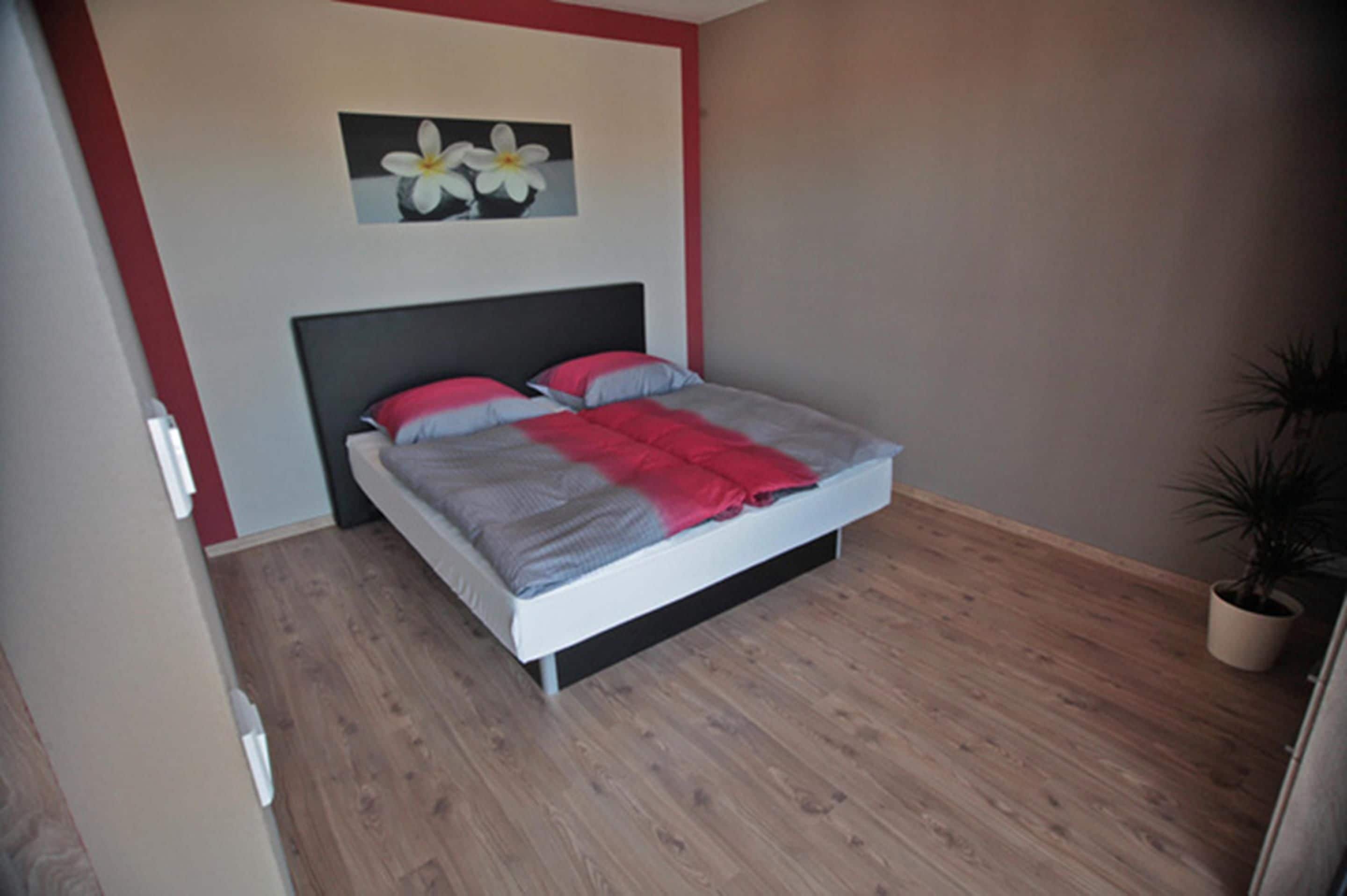 Een slaapkamer met een bed, een aan de muur hangend schilderij en een potplant.
