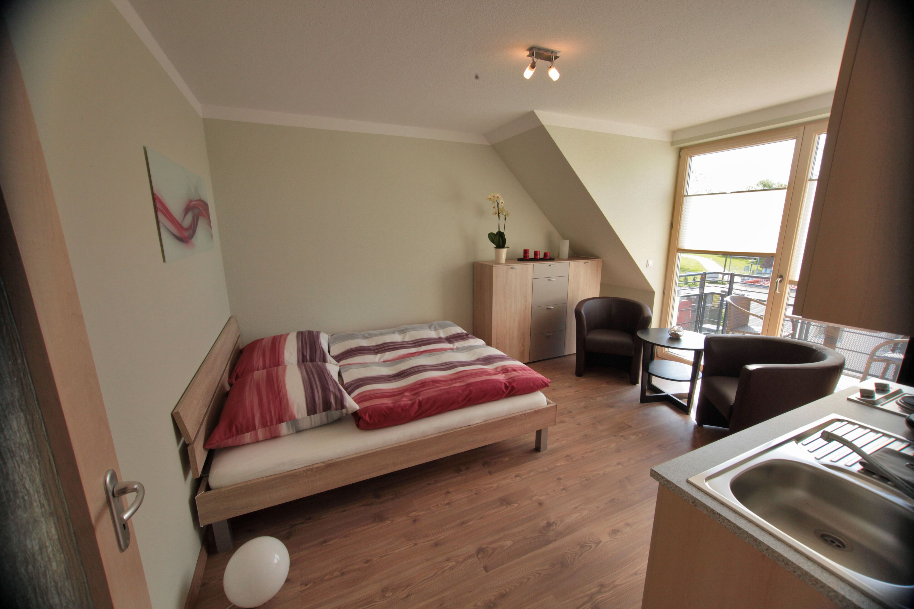 Een slaapkamer met een bed, een bureau, een stoel en een kitchenette.