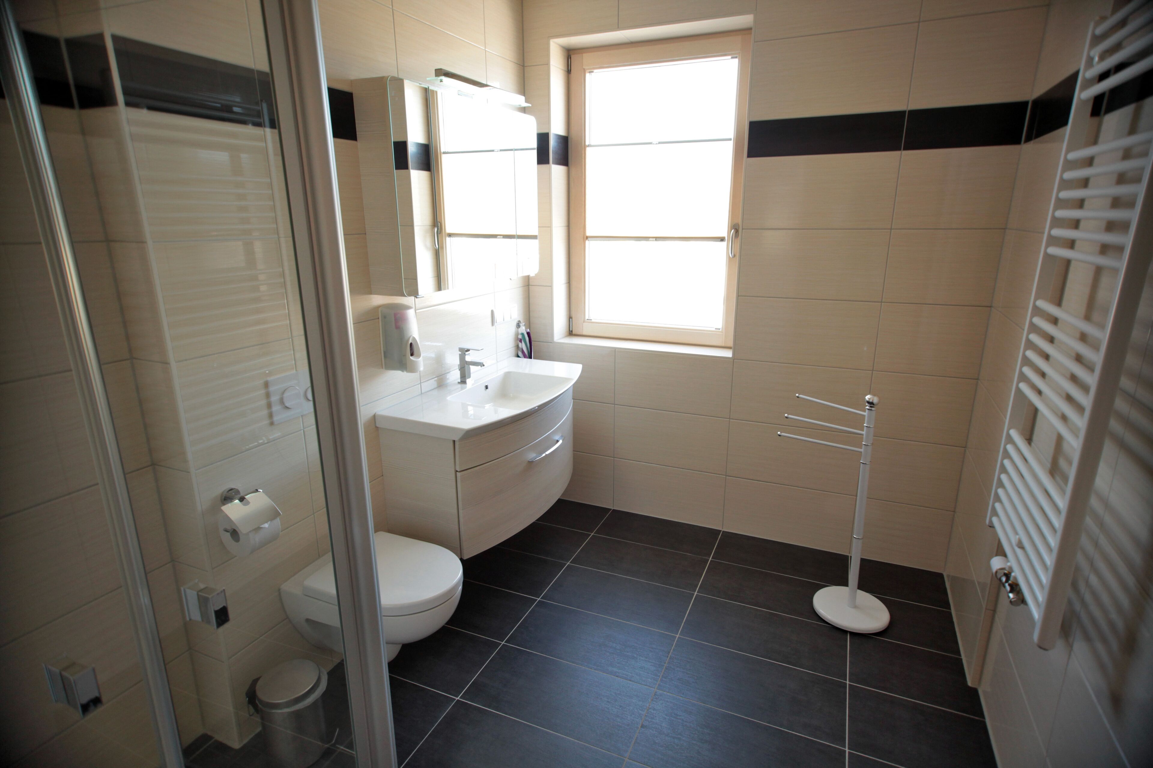 A bathroom with a toilet, sink, and mirror. There is a window providing natural light and a towel rack.