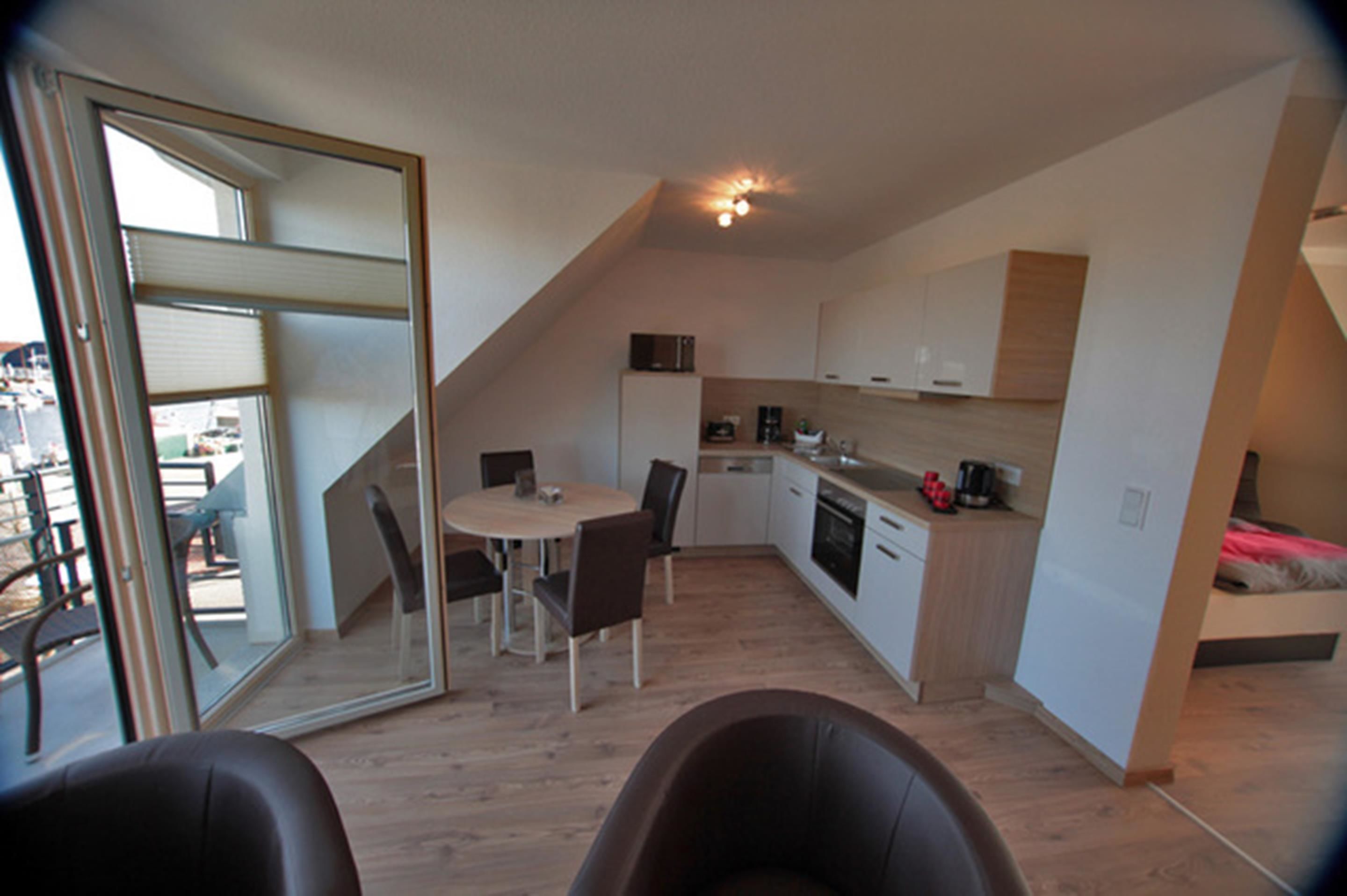 A compact kitchen with a dining area, a small kitchenette, and a bed in a loft-style room.