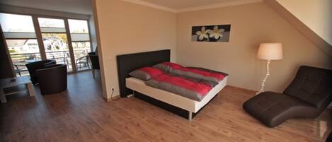 Un dormitorio con cama, una silla, una lámpara y vistas al exterior.