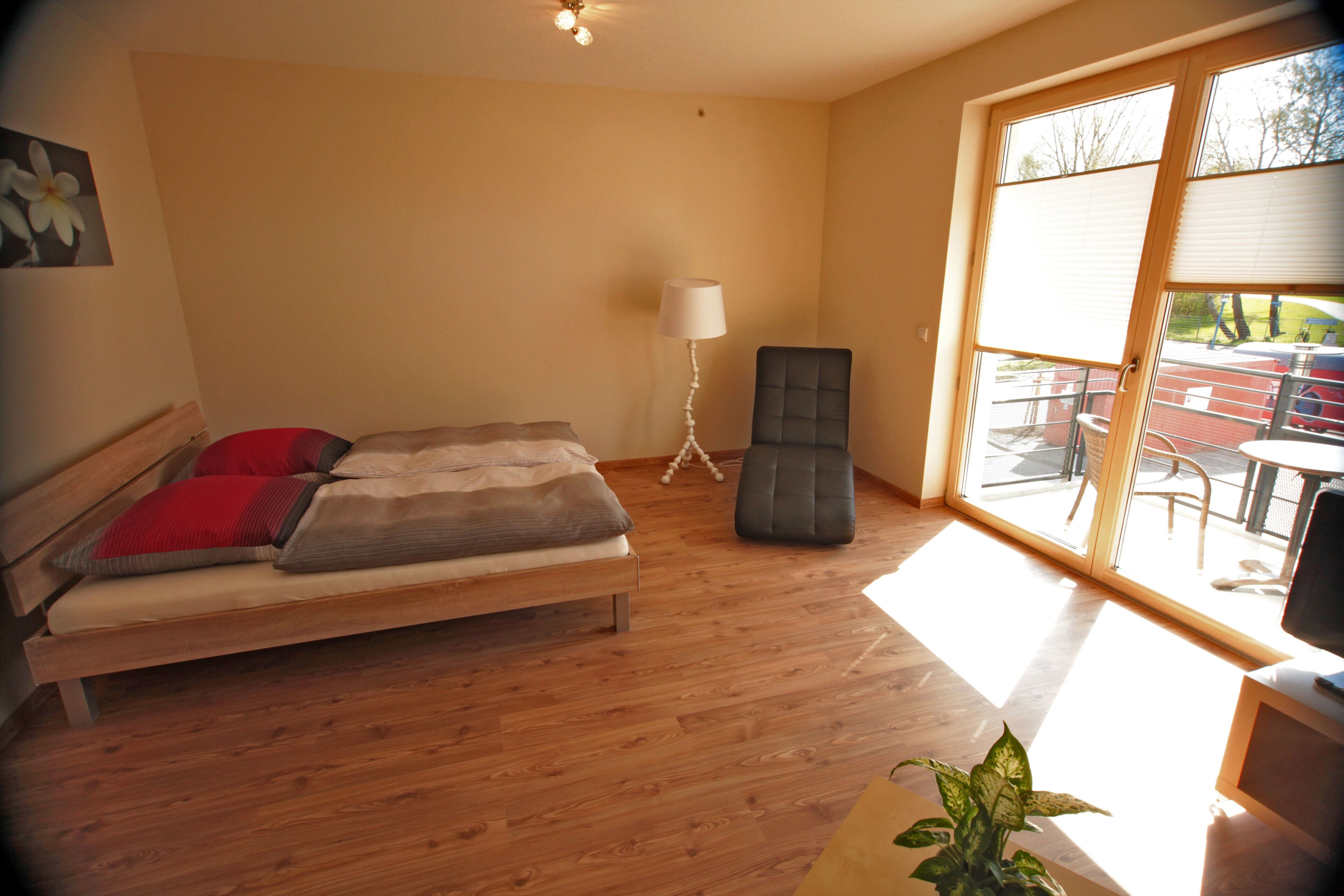 A bedroom with a bed, a floor lamp, and a view of the outside.