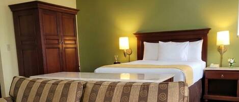 A hotel room with a bed, two bedside lamps, a wooden wardrobe, and a striped sofa.