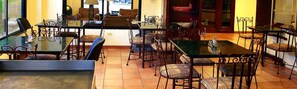 Un comedor con mesas y sillas de vidrio, piso de baldosas y vista a la calle.