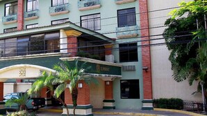 Un hotel de varios pisos con fachada verde, una entrada central con arco decorativo y varios balcones.