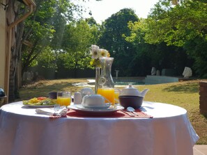 Une table de petit-déjeuner installée à l’extérieur, avec vue sur un jardin et une piscine.