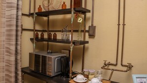 Una cocina con microondas, cafetera y estantes con frascos y un florero.