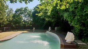Una piscina con borde de piedra, rodeada de árboles y una estatua.