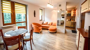 A modern living room with a sofa, a dining table with chairs, and a kitchen area visible through an open door. - Apartamenty Sun & Snow Kraszewskiego (Krynica-Zdroj)
