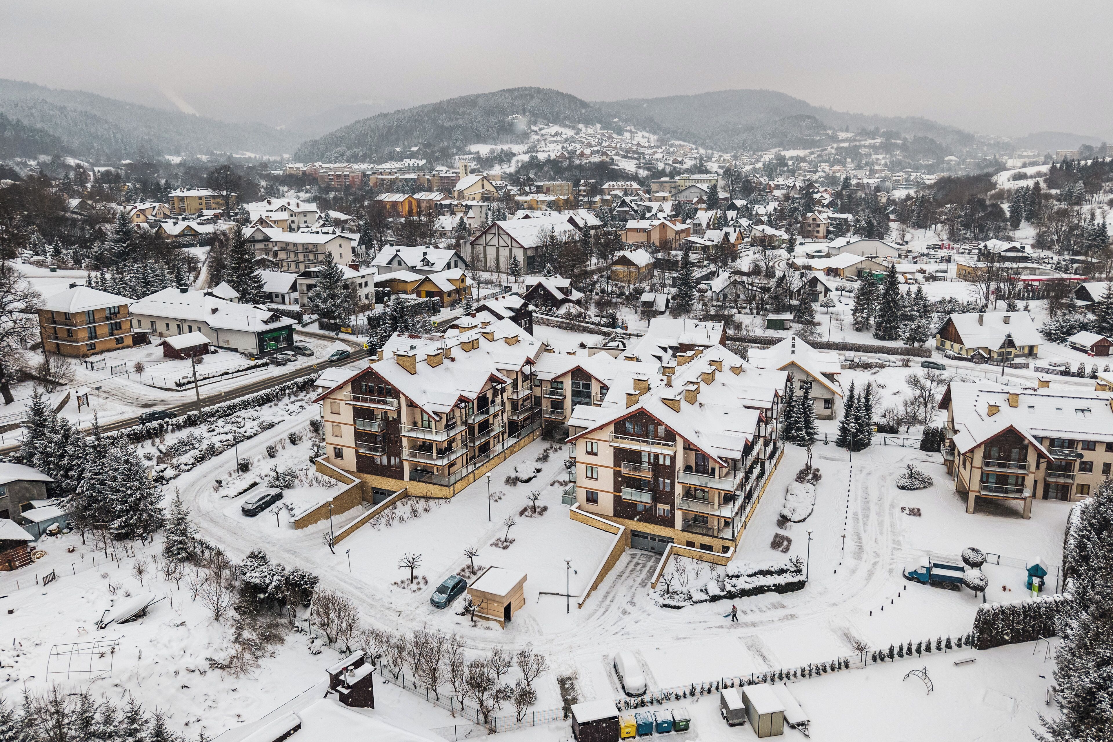Zona residenziale innevata con edifici a più piani, tra cui un hotel in evidenza con un ampio balcone e una funivia visibile sullo sfondo.