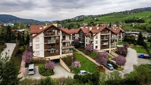 A multi-story residential building with balconies, surrounded by greenery and a hilly landscape. - Apartamenty Sun & Snow Kraszewskiego (Krynica-Zdroj)