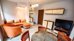 A modern living room with a sofa, TV, and dining area. - Apartamenty Sun & Snow Kraszewskiego (Krynica-Zdroj)