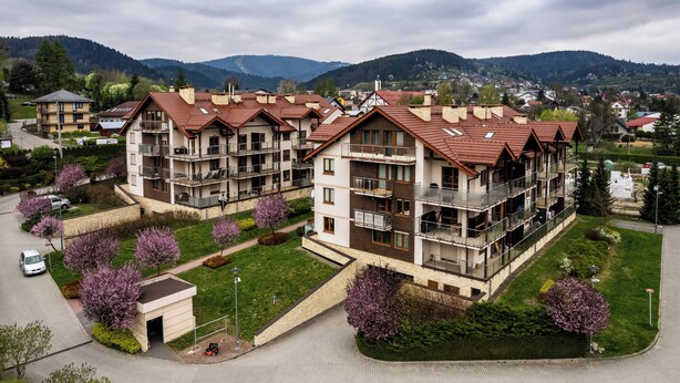 A multi-story residential building with balconies, surrounded by green lawns and flowering trees. - Apartamenty Sun & Snow Kraszewskiego (Krynica-Zdroj)